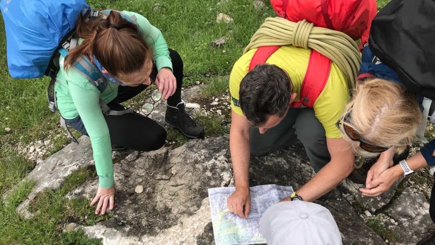 Vier Personen studieren eine Karte auf Felsuntergrund, darunter Guide Markus Schubert mit Kletterseil.