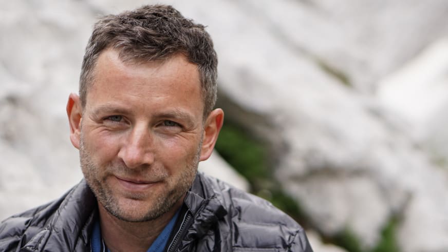 Guide Markus Schubert lächelt in die Kamera vor einer hellen Kalksteinwand mit grüner Vegetation.
