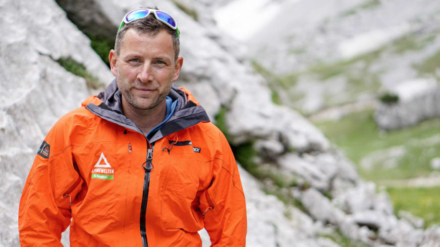 Guide Markus Schubert trägt orange Softshell-Jacke und blaue Gletscherbrille vor Kalksteinformationen.