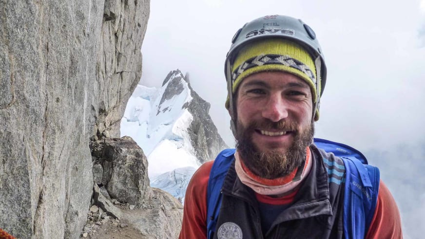 In hochalpiner Umgebung lächelt Bergführer Philipp Berg mit grauer Mütze und orange-schwarzer Jacke in die Kamera.