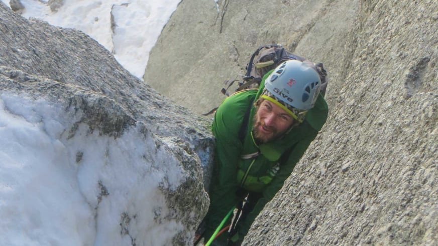 Beim Klettern an grau-beigem Fels greift Bergführer Philipp Berg aktiv in eine Felsritze und lächelt in die Kamera.