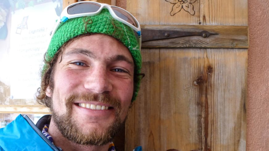 Bergführer Philipp Berg lächelt in die Kamera und trägt grüne Strickmütze und Skibrille auf dem Kopf.
