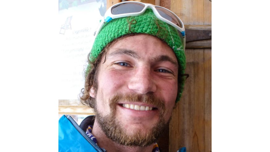 Lächelnder Bergführer Philipp Berg trägt grüne gestrickte Mütze und weiße Skibrille auf dem Kopf in Hütteninnenraum.