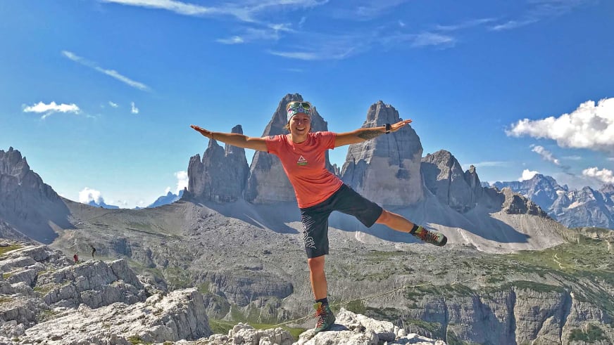 Bergwanderführerin Sandra Wolf steht in Yoga-Pose mit ausgestreckten Armen auf einem Felsblock vor hohen Kalksteintürmen.