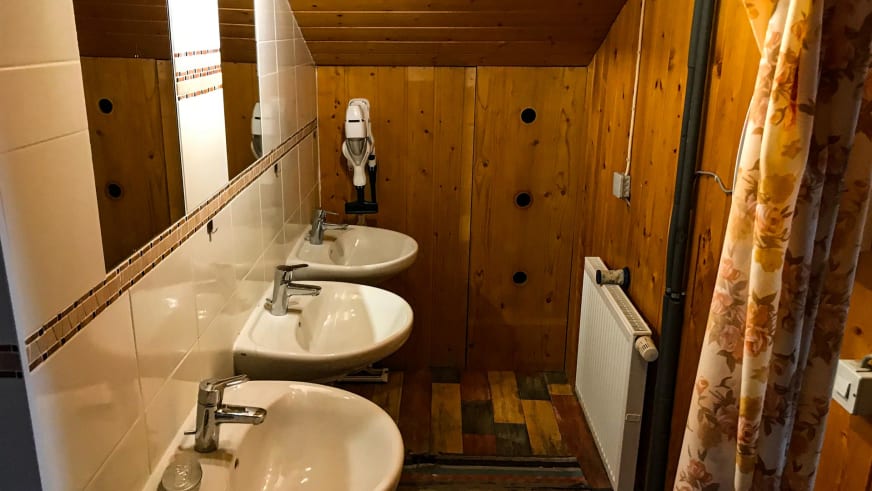 Waschraum mit drei weißen Waschbecken und gefliesten Wänden im Tegelberghaus.