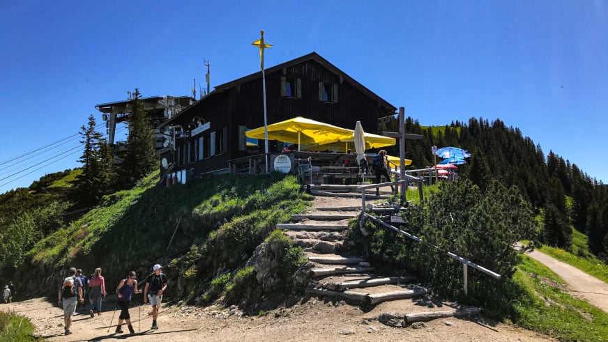 Wandergruppe mit Rucksäcken auf dem Weg zum Tegelberghaus auf dem bewaldeten Gipfel.