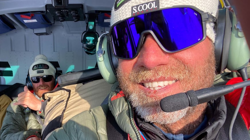 Bergführer Christian Knabe sitzt im Hubschrauber mit Headset und blonder Skibrille, dahinter eine zweite Person mit Sonnenbrille.
