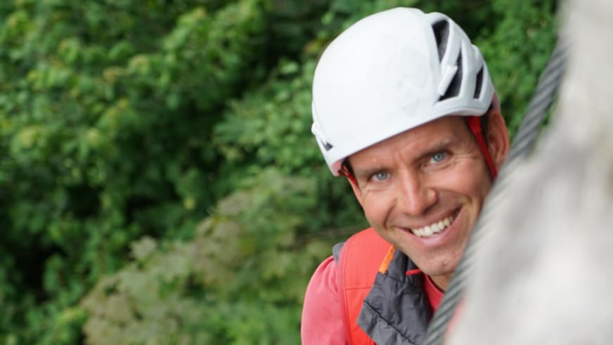 Bergführer Christian Knabe lächelt in die Kamera und trägt weißen Kletterhelm sowie rote Outdoorjacke.