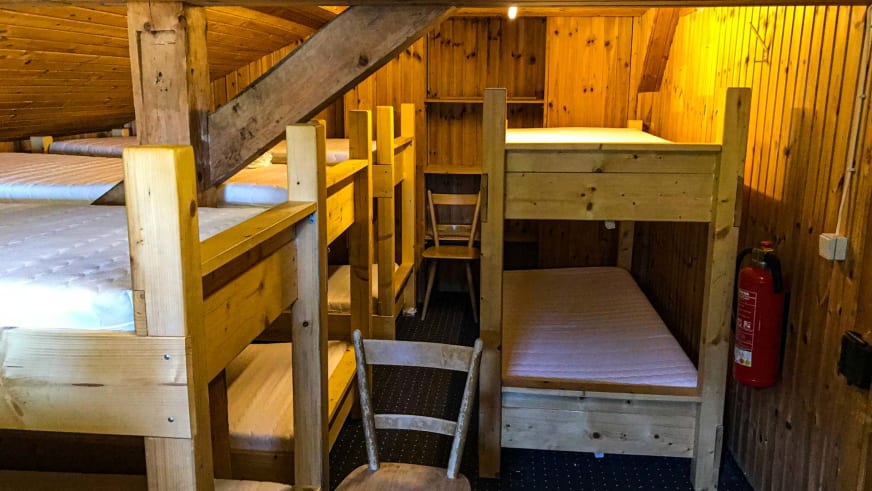 Schlafsaal mit mehreren Etagenbetten aus Holz unter dem Dachstuhl des Tegelberghaus.