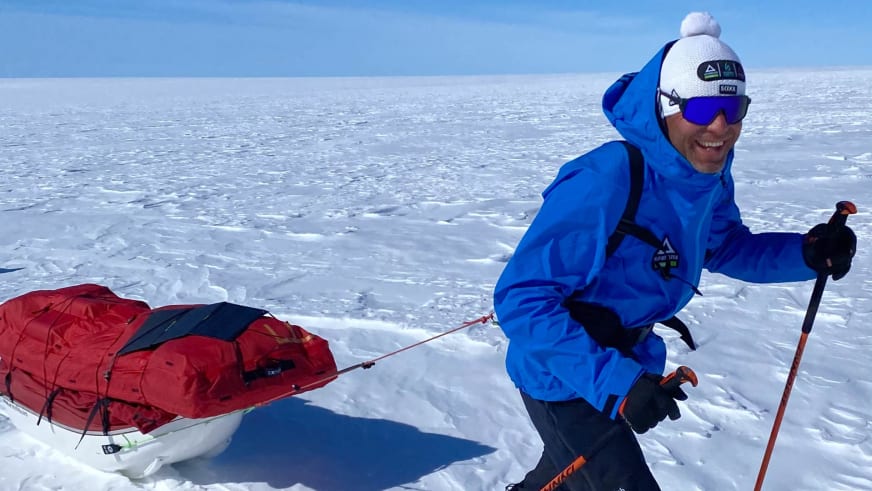 Über weite Eisfläche in Grönland zieht Bergführer Christian Knabe einen roten Expeditionsschlitten mit Ausrüstung.