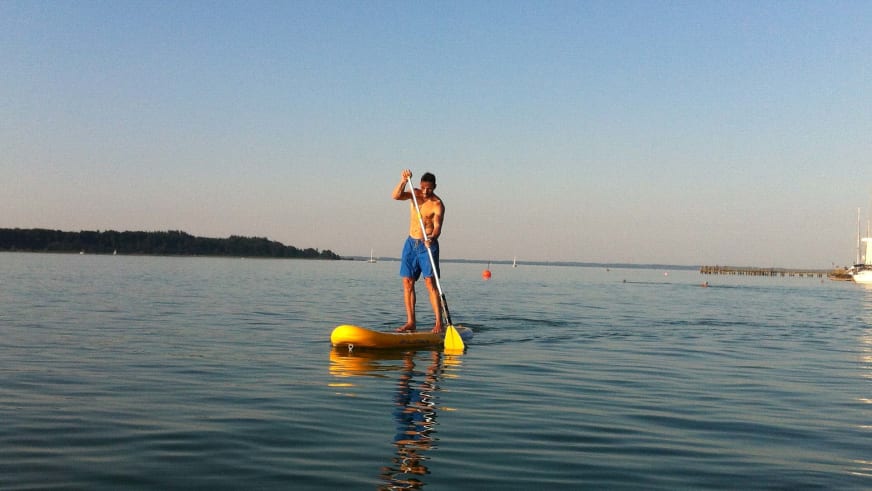 Auf gelbem Stand-Up-Paddle-Board steht Bergführer Rene Hellmann mit Paddel bei goldenem Abendlicht auf ruhigem Wasser.