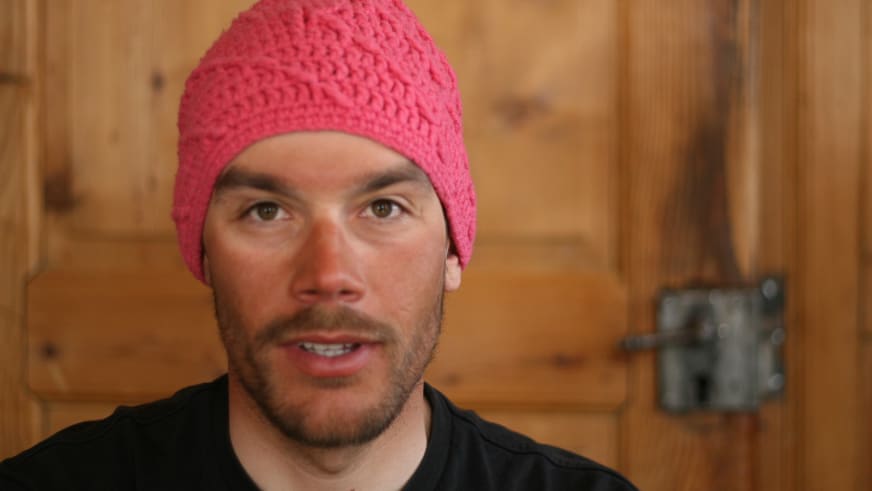 Portrait zeigt Philipp Neumann als Bergführer mit pink-roter Wollmütze vor Holzwänden in warmem Licht.
