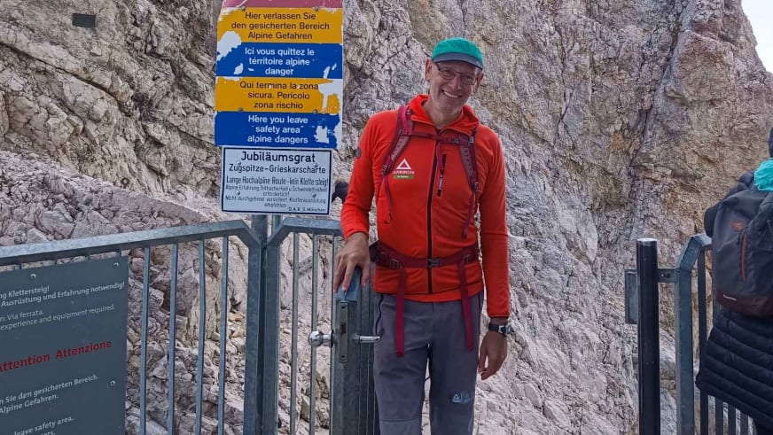 Bergwanderführer Manfred Beier steht in roter Jacke und grüner Mütze lächelnd am Metallgeländer vor hellem Kalksteinfels der Zugspitze.