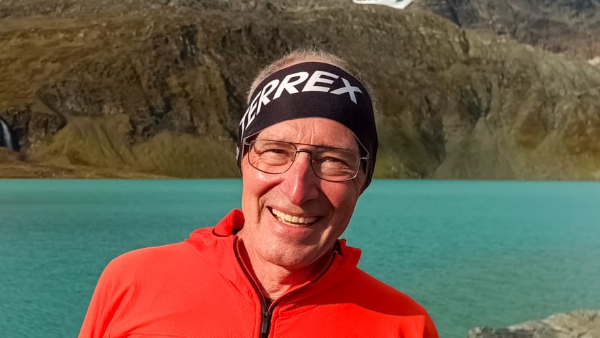 Portrait von Bergwanderführer Manfred Beier mit Brille und Stirnband vor türkisfarbenem Bergsee und steilen Felswänden.