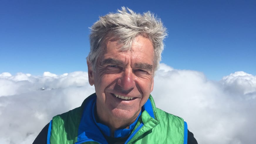 Bergführer Walter Kern lächelt in grüner Softshell-Jacke vor einer weißen Wolkendecke und blauem Himmel.