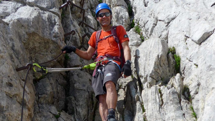 Bergwanderführer Andreas Schneider mit blauem Helm und Klettersteig-Set klettert an heller Kalksteinwand mit Drahtseilen und Stahltritten.