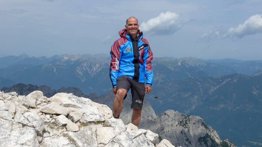 Bergwanderführer Andreas Schneider in blau-roter Outdoorjacke steht auf hellem Kalksteingestein mit Bergpanorama im Hintergrund.