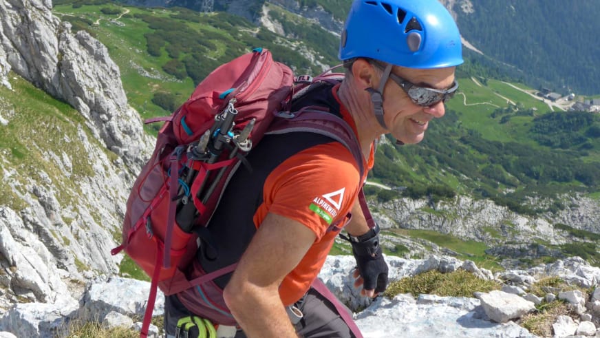 Bergwanderführer Andreas Schneider mit blauem Helm und rotem Rucksack klettert über helle Kalksteinfelsen mit Blick ins Tal.