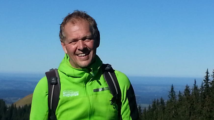 Portrait von Bergwanderführer Martin Werner in grüner Zugspitze-Jacke mit Rucksack vor weiter Berglandschaft.