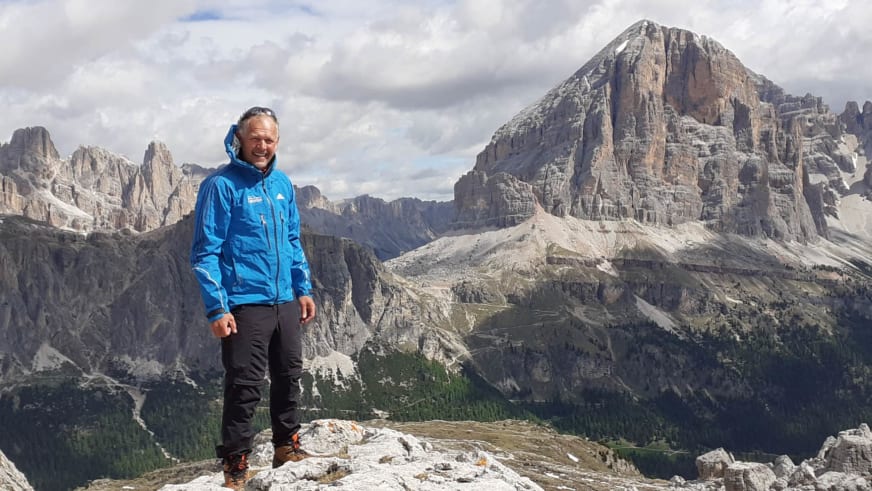 Bergwanderführer Martin Werner in blauer Softshell-Jacke auf felsigem Plateau vor hohen Dolomiten-Felswänden.
