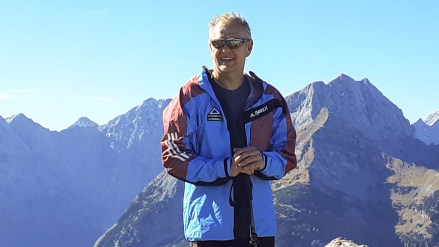 Vor schneebedeckten Gipfeln steht Bergwanderführer Martin Werner in blauer Funktionsjacke mit verschränkten Armen.