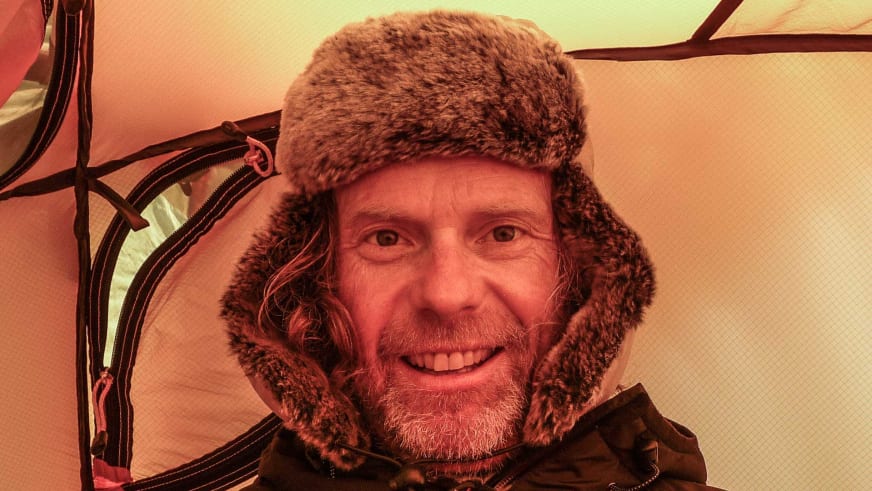 Bergführer Andreas Bucher trägt eine braune Fellmütze mit Ohrenklappen und lächelt in warmer Innenraumbeleuchtung.