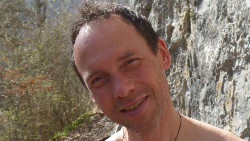 Klettertrainer Volker Wild lächelt vor einer strukturierten Felswand mit grauen und gelblichen Gesteinsfarben.
