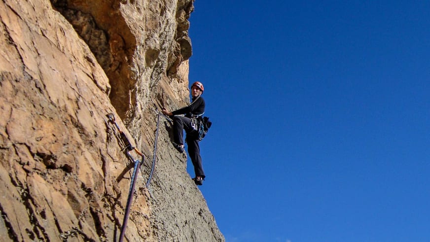 An einer gelblich-braunen Felswand klettert Bergführer Peter Klug mit rotem Helm und schwarzer Kleidung aufwärts.