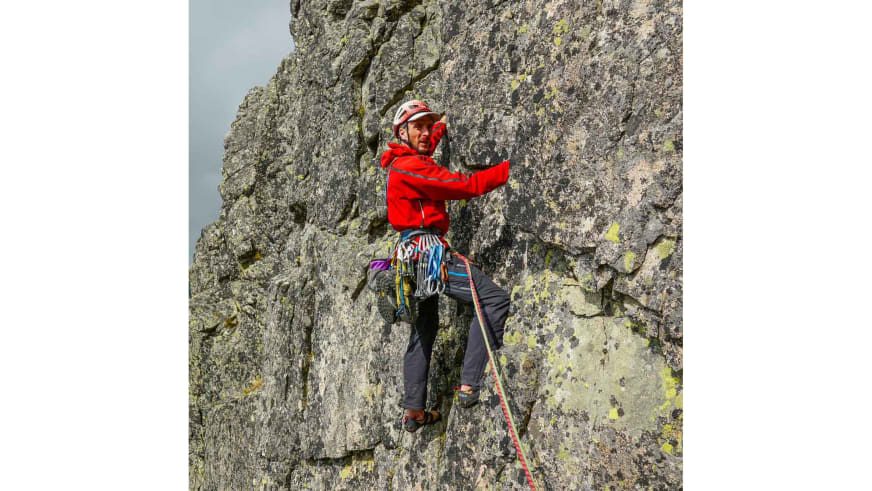 In roter Softshelljacke und weißem Helm klettert Bergführer Peter Klug an einer steilen Felswand aus grauem Gestein.