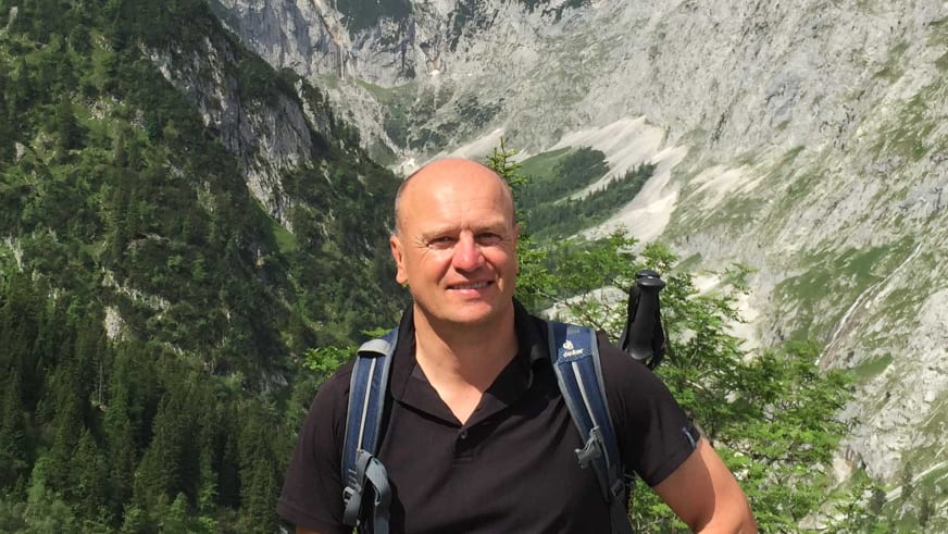 Mit schwarzem Poloshirt und blauem Wanderrucksack steht Bergwanderführer Peter Kohl vor einem tiefen Tal mit steilen Kalksteinwänden.