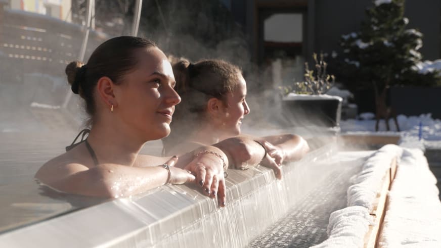 Gäste entspannen im Außen-Whirlpool des Hotel Bär & Post Zernez bei warmem Dampf und goldenem Licht.