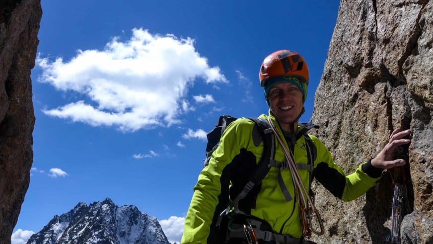 Bergführer Martin Schidlowski lächelt in orangem Kletterhelm und grüner Softshell-Jacke vor Kalkstein-Felswand.