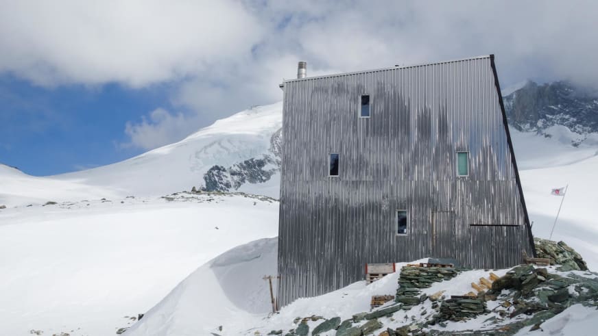 Die Cabane Tracuit steht auf felsigem Untergrund zwischen Schneefeldern und vergletscherten Gipfeln der Walliser Alpen.