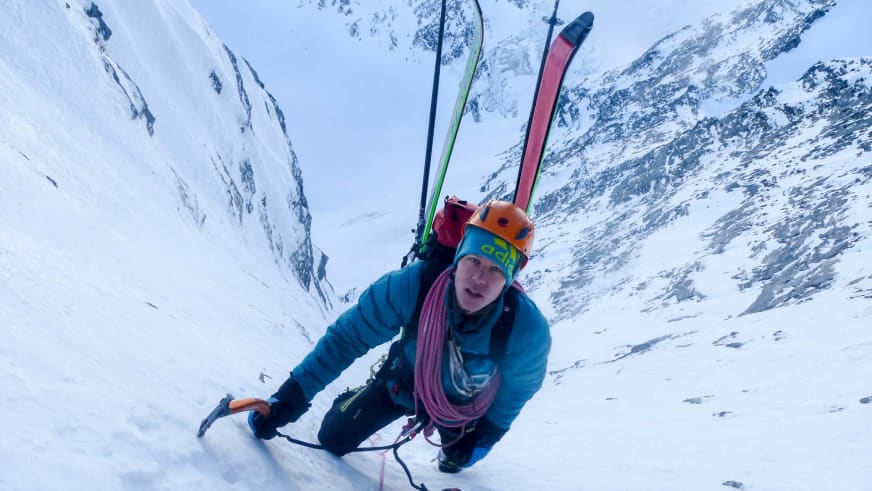 Bergführer Martin Schidlowski kniet mit Eispickel in blauer Daunenjacke im Neuschnee, zwei Skier stehen neben ihm im Schnee.