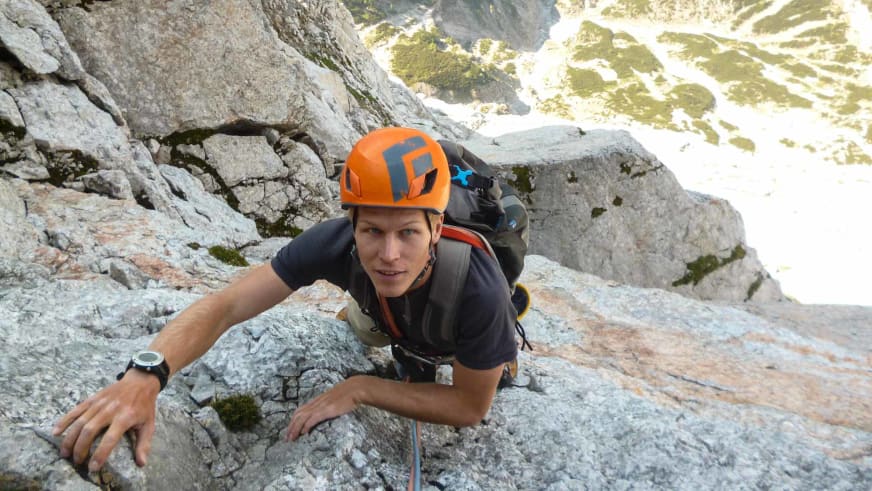 Bergführer Martin Schidlowski klettert aktiv an grauer Kalkstein-Felswand mit orangem Helm und rotem Kletterseil.