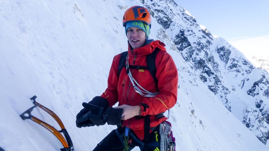 Mit zwei gelben Eisgeräten steht Bergführer Martin Schidlowski in roter Softshell-Jacke vor verschneiten Felswänden.