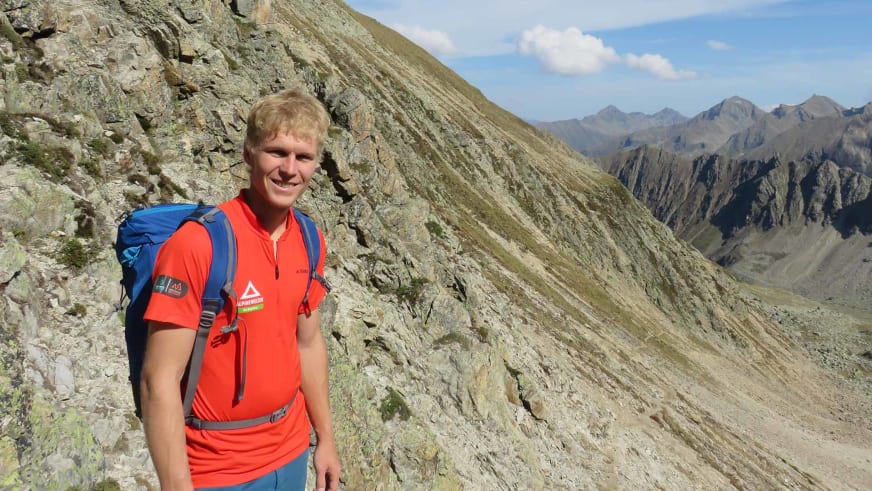 Bergführer Martin Schidlowski steht beim Hochtourenkurs mit rotem Alpine Welten Shirt auf hellem Felsgrat.