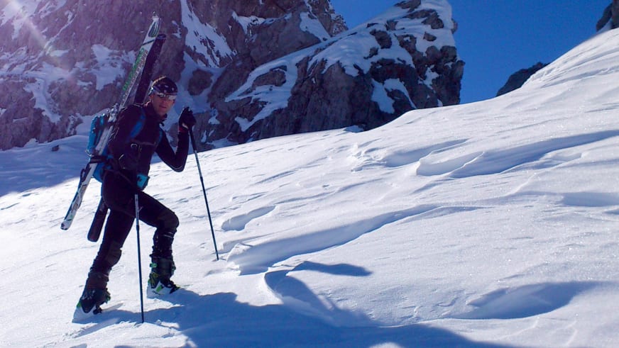Bergführer Michael Aigner steigt mit Tourenskiern durch tiefen Pulverschnee auf, verschneite Felswände im Hintergrund sichtbar.