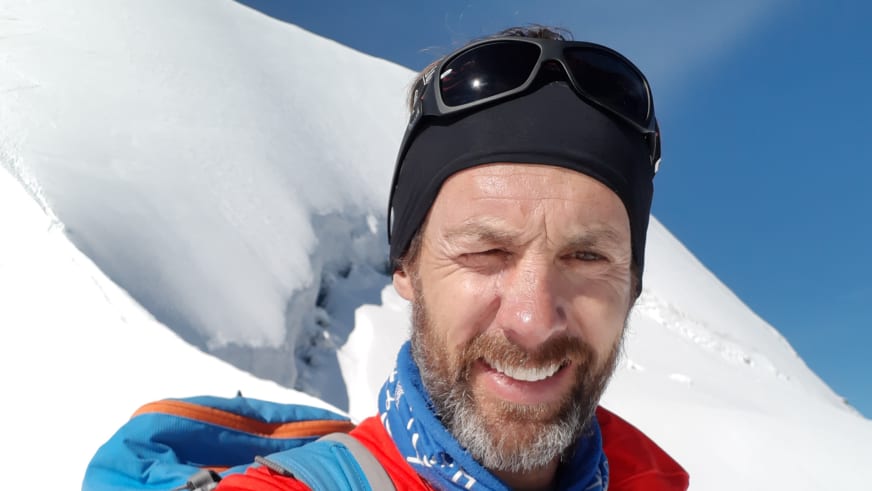 Portrait von Bergführer Michael Aigner mit Gletscherbrille und grauem Bart am Berner Dreigestirn bei strahlendem Sonnenschein.