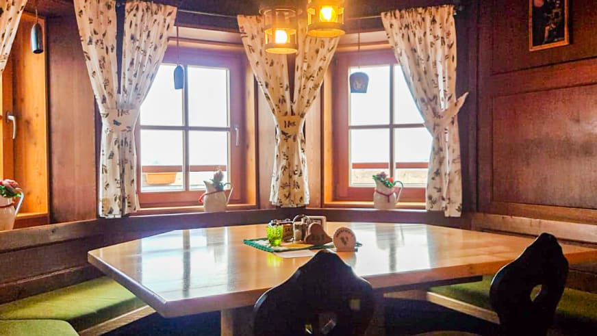 Gastraum im Ingolstädter Haus mit Holztisch, grünen Sitzpolstern und drei Glaslaternen als Beleuchtung.