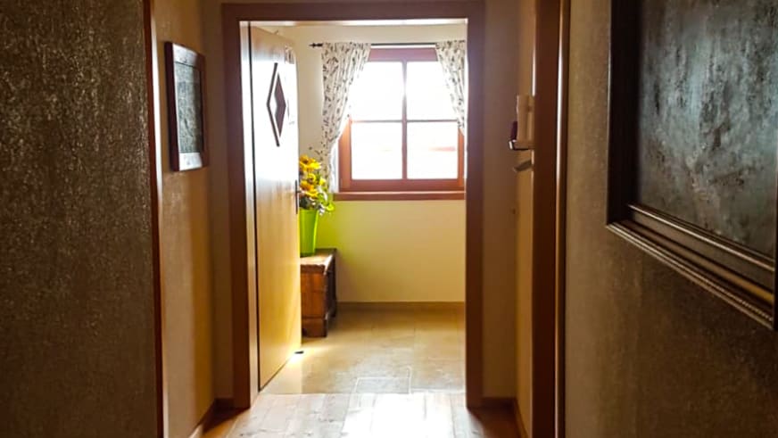 Flur im Ingolstädter Haus mit hellen Steinplatten und Blick durch Holztür in angrenzenden Raum.