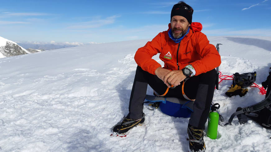 Bergführer Michael Aigner macht Pause im Schnee während einer Hochtour am Großvenediger mit Ausrüstung und blauem Rucksack.