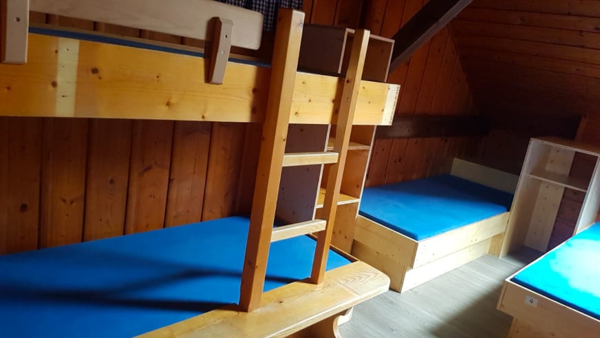 Schlafraum im Ingolstädter Haus mit Etagenbetten aus hellem Holz und blauer Bettwäsche an Holzwänden.