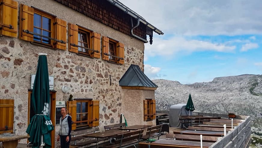 Terrasse des Ingolstädter Haus mit Bierbänken und orangefarbenen Fensterläden vor Bergpanorama.