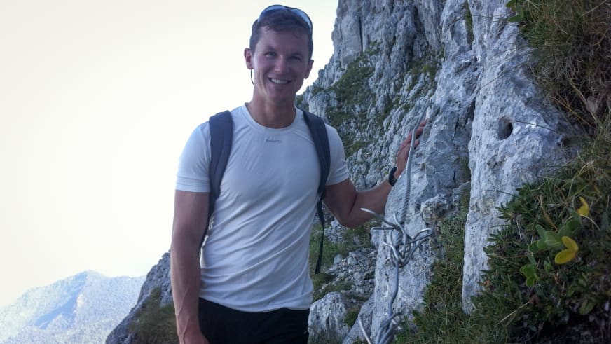 Bergführer Harald Hosner steht lächelnd vor einer grauen Kalksteinwand und berührt mit der Hand den strukturierten Fels.