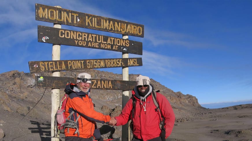 Am Kilimanjaro-Gipfelschild des Stella Point geben sich Bergwanderführer Werner Neubauer und ein Begleiter die Hand auf 5756m Höhe.
