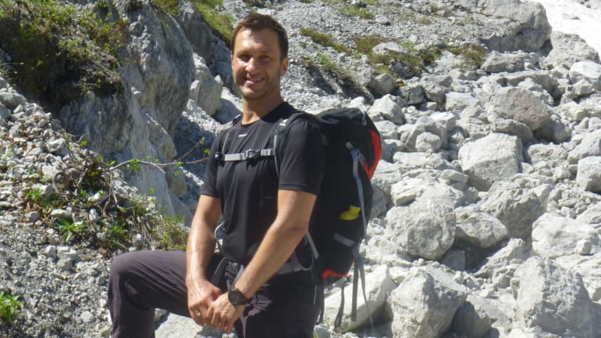 Entspannt sitzt Bergwanderführer Andreas Maier auf einem Felsblock in karstiger Gerölllandschaft aus hellem Kalkstein.