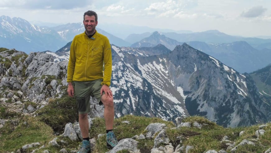 Auf einem Berggipfel im Nationalpark Berchtesgaden lächelt Bergwanderführer Michael Lichtenstern in gelber Jacke.