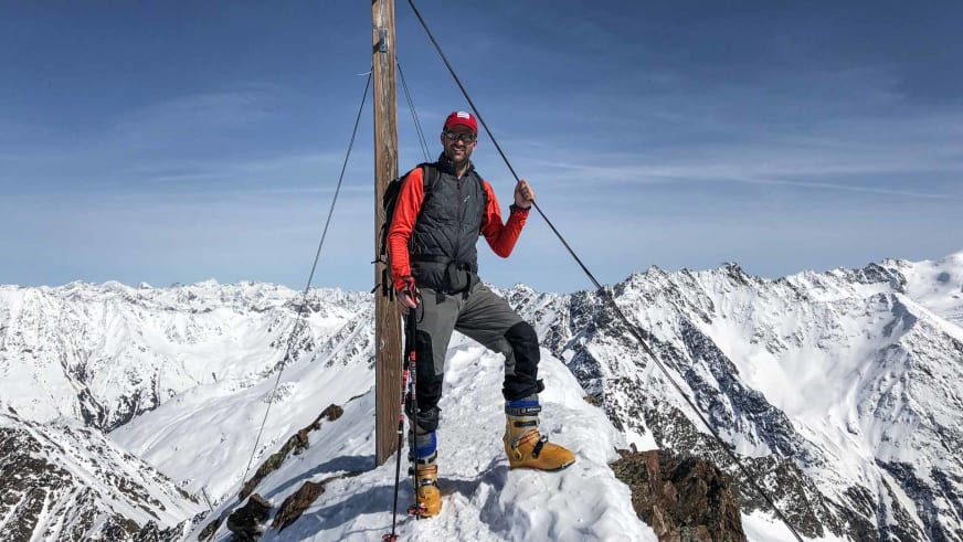 Bergwanderführer Michael Lichtenstern steht mit Skiern am Gipfelkreuz der Wildspitze bei strahlendem Sonnenschein.