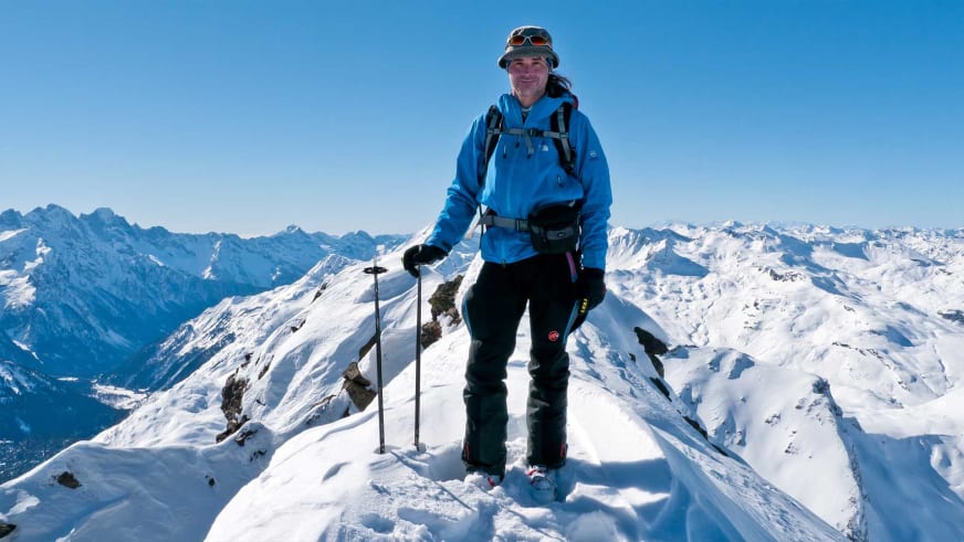 Auf einem schneebedeckten Gipfelgrat steht Bergwanderführer Markus Arndt mit Eisäxten am Klettergurt.